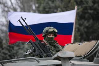 A pro-Russian man (not seen) holds a Russian flag behind an armed servicemen on top of a Russian army vehicle outside a Ukrainian border guard post in the Crimean town of Balaclava March 1, 2014. Ukraine accused Russia on Saturday of sending thousands of extra troops to Crimea and placed its military in the area on high alert as the Black Sea peninsula appeared to slip beyond Kiev's control. REUTERS/Baz Ratner (UKRAINE - Tags: MILITARY POLITICS CIVIL UNREST) - RTR3FVD5